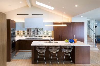 Mid-sized trendy l-shaped light wood floor and beige floor open concept kitchen photo in San Francisco with an undermount sink, flat-panel cabinets, dark wood cabinets, solid surface countertops, metallic backsplash, mirror backsplash, paneled appliances and an island