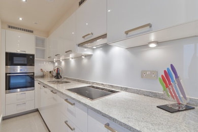 Photo of a small modern galley kitchen in London with a submerged sink, white cabinets, glass sheet splashback, black appliances, porcelain flooring, grey floors and white worktops.