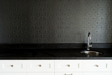 Inredning av ett klassiskt kök och matrum, med en undermonterad diskho, luckor med infälld panel, vita skåp, granitbänkskiva, svart stänkskydd, stänkskydd i sten, rostfria vitvaror och travertin golv