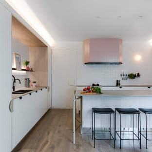 Photo of a mid-sized contemporary l-shaped open plan kitchen in Sydney with a double-bowl sink, white cabinets, recycled glass benchtops, white splashback, cement tile splashback, black appliances, medium hardwood floors, with island, grey benchtop, flat-panel cabinets and brown floor.