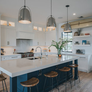 This is an example of a mid-sized beach style open plan kitchen in Other with a single-bowl sink, louvered cabinets, white cabinets, onyx benchtops, yellow splashback, stone slab splashback, stainless steel appliances, light hardwood floors, with island and brown floor.