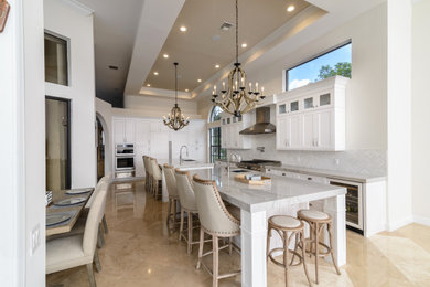 Inspiration for an expansive mediterranean l-shaped kitchen/diner in Miami with a submerged sink, shaker cabinets, white cabinets, white splashback, integrated appliances, multiple islands, beige floors and grey worktops.