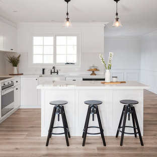 Inspiration for a mid-sized transitional l-shaped open plan kitchen in Sydney with a farmhouse sink, shaker cabinets, white cabinets, marble benchtops, white splashback, marble splashback, stainless steel appliances, laminate floors, with island, brown floor and white benchtop.