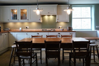 На фото: большая угловая кухня в стиле кантри с обеденным столом, фасадами в стиле шейкер, деревянной столешницей, полом из сланца и разноцветным полом с
