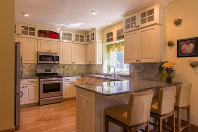 Mid-sized elegant u-shaped medium tone wood floor and brown floor eat-in kitchen photo in Milwaukee with an undermount sink, raised-panel cabinets, white cabinets, granite countertops, beige backsplash, terra-cotta backsplash, stainless steel appliances and a peninsula