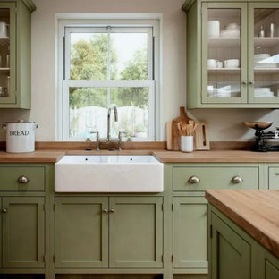 Photo of a mid-sized contemporary l-shaped eat-in kitchen in Columbus with a farmhouse sink, recessed-panel cabinets, green cabinets, wood benchtops, brown splashback, timber splashback, stainless steel appliances, medium hardwood floors, with island, brown floor and brown benchtop.