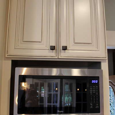 Example of a mid-sized transitional galley medium tone wood floor eat-in kitchen design in Cleveland with a farmhouse sink, raised-panel cabinets, white cabinets, granite countertops, brown backsplash, brick backsplash, stainless steel appliances and an island