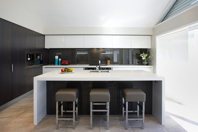 Inredning av ett modernt kök och matrum, med glaspanel som stänkskydd, en köksö och svart stänkskydd