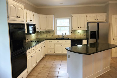 Example of a classic kitchen design in Charlotte with raised-panel cabinets, white cabinets, beige backsplash, stone tile backsplash, black appliances and an island
