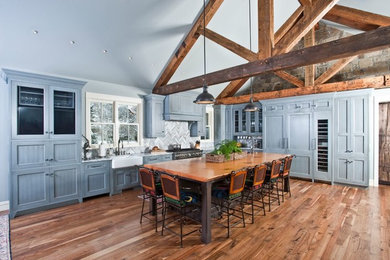 Example of a large mountain style l-shaped medium tone wood floor and brown floor eat-in kitchen design in Other with a farmhouse sink, recessed-panel cabinets, granite countertops, gray backsplash, stone tile backsplash, stainless steel appliances, an island and gray cabinets