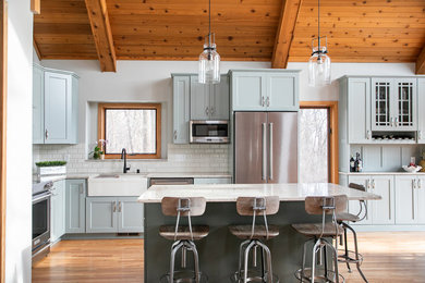 Mountain style l-shaped medium tone wood floor kitchen photo in Other with a farmhouse sink, shaker cabinets, gray cabinets, white backsplash, subway tile backsplash, stainless steel appliances, an island and white countertops