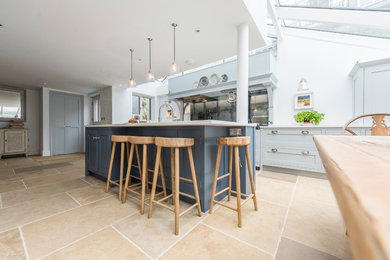 This is an example of a large contemporary kitchen in Cornwall with a belfast sink, shaker cabinets, grey cabinets, engineered stone countertops, metallic splashback, glass sheet splashback, integrated appliances, porcelain flooring and an island.