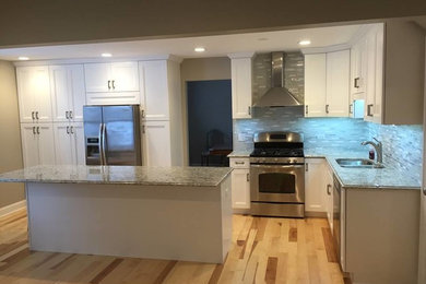 Example of a mid-sized transitional l-shaped light wood floor kitchen design in Chicago with a double-bowl sink, recessed-panel cabinets, white cabinets, multicolored backsplash, matchstick tile backsplash, stainless steel appliances and an island