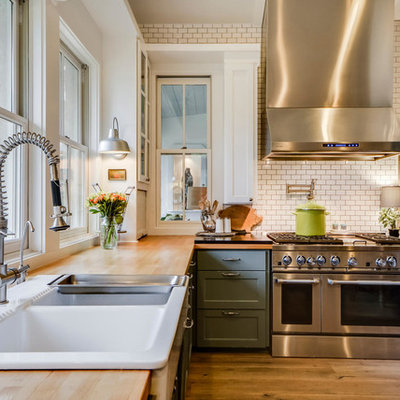Example of a cottage light wood floor kitchen design in Austin with a farmhouse sink, shaker cabinets, green cabinets, wood countertops, white backsplash, subway tile backsplash and stainless steel appliances