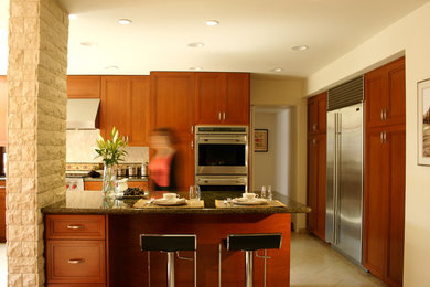 Cette photo montre une cuisine chic en bois brun de taille moyenne avec un placard à porte shaker, un plan de travail en granite et un électroménager en acier inoxydable.