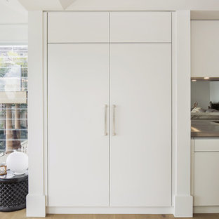 This is an example of a large modern single-wall open plan kitchen in Sydney with an integrated sink, flat-panel cabinets, beige cabinets, marble benchtops, metallic splashback, mirror splashback, black appliances, light hardwood floors and with island.