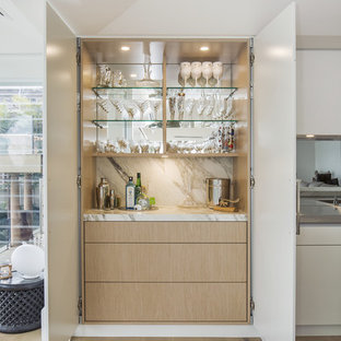 This is an example of a large modern single-wall open plan kitchen in Sydney with an integrated sink, flat-panel cabinets, beige cabinets, marble benchtops, metallic splashback, mirror splashback, black appliances, light hardwood floors and with island.