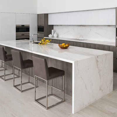 Kitchen - contemporary beige floor kitchen idea in Los Angeles with an undermount sink, flat-panel cabinets, white cabinets, white backsplash, stone slab backsplash, paneled appliances, an island and white countertops