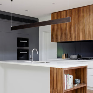 Design ideas for a mid-sized contemporary galley open plan kitchen in Melbourne with an undermount sink, flat-panel cabinets, white cabinets, solid surface benchtops, black splashback, glass sheet splashback, panelled appliances, medium hardwood floors, with island and white benchtop.