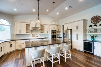 Open concept kitchen - mid-sized modern l-shaped medium tone wood floor and brown floor open concept kitchen idea with an undermount sink, shaker cabinets, white cabinets, white backsplash, mosaic tile backsplash, stainless steel appliances, an island and gray countertops