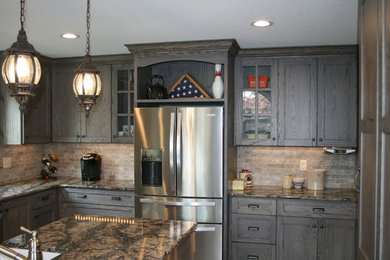 Example of a mid-sized classic l-shaped dark wood floor eat-in kitchen design in Other with a farmhouse sink, shaker cabinets, distressed cabinets, granite countertops, gray backsplash, stone tile backsplash, stainless steel appliances and an island