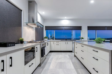 Bild på ett funkis grå grått kök, med en dubbel diskho, vita skåp, bänkskiva i kvarts, vitt stänkskydd, stänkskydd i porslinskakel, rostfria vitvaror, klinkergolv i porslin, en köksö och grått golv