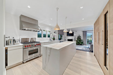 Example of a mid-sized trendy single-wall light wood floor and brown floor open concept kitchen design in San Francisco with an undermount sink, flat-panel cabinets, white cabinets, marble countertops, white backsplash, stone slab backsplash, white appliances, an island and white countertops