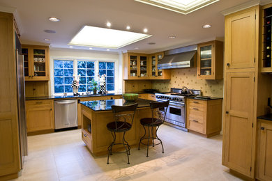 Photo of a large traditional u-shaped kitchen/diner in San Francisco with shaker cabinets, light wood cabinets, granite worktops, beige splashback, stainless steel appliances, ceramic flooring, a double-bowl sink, glass tiled splashback, an island, brown floors and black worktops.