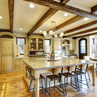 This is an example of a large country u-shaped open plan kitchen in Los Angeles with a farmhouse sink, beaded inset cabinets, distressed cabinets, limestone benchtops, black appliances, light hardwood floors and with island.