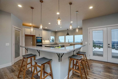 Example of a large minimalist u-shaped brown floor eat-in kitchen design in Seattle with a farmhouse sink, shaker cabinets, white cabinets, quartz countertops, white backsplash, marble backsplash, stainless steel appliances and two islands