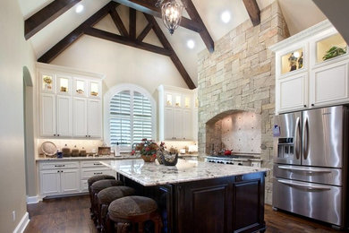 Inspiration for a large craftsman l-shaped dark wood floor and brown floor enclosed kitchen remodel in Austin with an undermount sink, raised-panel cabinets, white cabinets, quartz countertops, beige backsplash, limestone backsplash, stainless steel appliances and an island