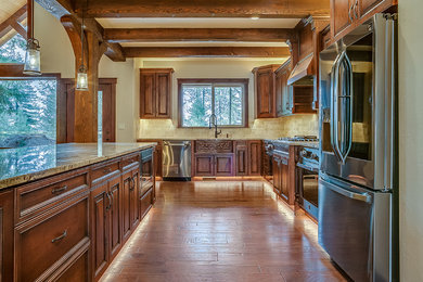 Inspiration for a mid-sized craftsman l-shaped dark wood floor and brown floor open concept kitchen remodel in Seattle with a farmhouse sink, raised-panel cabinets, dark wood cabinets, granite countertops, beige backsplash, ceramic backsplash, stainless steel appliances, an island and beige countertops