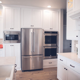 Mid-sized contemporary l-shaped open plan kitchen in Other with an undermount sink, shaker cabinets, white cabinets, marble benchtops, grey splashback, slate splashback, stainless steel appliances, light hardwood floors, with island and brown floor.