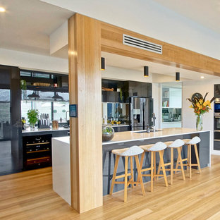 Inspiration for a contemporary l-shaped kitchen in Other with an undermount sink, flat-panel cabinets, grey cabinets, mirror splashback, stainless steel appliances, light hardwood floors, with island, brown floor and white benchtop.