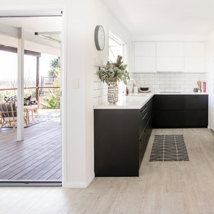 Beach style u-shaped kitchen in Sunshine Coast with an undermount sink, flat-panel cabinets, black cabinets, white splashback, subway tile splashback, stainless steel appliances, light hardwood floors, no island, beige floor and white benchtop.
