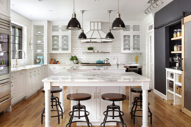 Inspiration for a large timeless l-shaped medium tone wood floor kitchen remodel in New York with marble countertops, white backsplash, subway tile backsplash, stainless steel appliances, white countertops, two islands, an undermount sink and shaker cabinets
