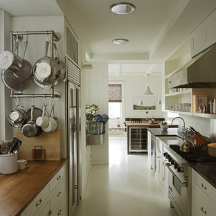 Photo of a modern galley separate kitchen in New York with wood benchtops, a farmhouse sink, open cabinets, white cabinets, stainless steel appliances and white floor.