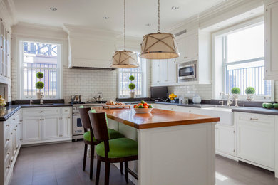 Example of a mid-sized classic u-shaped kitchen design in New York with a farmhouse sink, shaker cabinets, white cabinets, white backsplash, subway tile backsplash, stainless steel appliances and an island