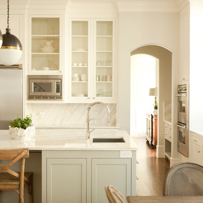 Eat-in kitchen - traditional eat-in kitchen idea in Dallas with glass-front cabinets, stainless steel appliances, white cabinets, white backsplash and stone slab backsplash
