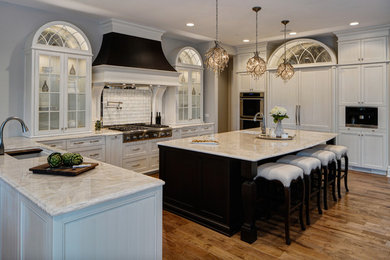 Large transitional u-shaped medium tone wood floor and brown floor open concept kitchen photo in Chicago with an undermount sink, recessed-panel cabinets, white cabinets, quartzite countertops, white backsplash, glass tile backsplash, paneled appliances, an island and white countertops