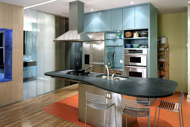 Example of a mid-sized eclectic single-wall medium tone wood floor and brown floor kitchen design in New York with a double-bowl sink, flat-panel cabinets, blue cabinets, soapstone countertops, stainless steel appliances and an island