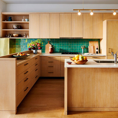 Mid-century modern u-shaped light wood floor and brown floor kitchen photo in New York with a drop-in sink, flat-panel cabinets, light wood cabinets, green backsplash and an island