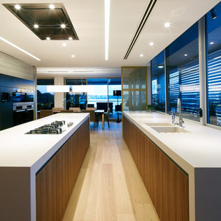 Photo of a modern galley kitchen in Sydney with an integrated sink, flat-panel cabinets, dark wood cabinets, concrete benchtops, window splashback, black appliances, light hardwood floors, with island, beige floor and grey benchtop.