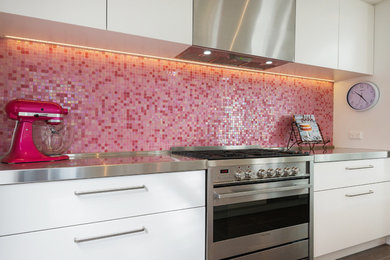 Photo of a small contemporary galley kitchen in Auckland with a submerged sink, flat-panel cabinets, white cabinets, composite countertops, pink splashback, mosaic tiled splashback, stainless steel appliances, ceramic flooring and an island.