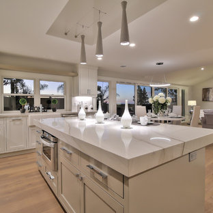 Inspiration for a modern l-shaped eat-in kitchen in San Francisco with a farmhouse sink, shaker cabinets, white cabinets, quartzite benchtops, white splashback, porcelain splashback, stainless steel appliances, light hardwood floors, with island and green floor.