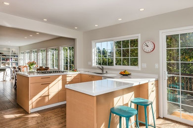 Example of a mid-sized minimalist u-shaped medium tone wood floor and brown floor open concept kitchen design in San Francisco with an undermount sink, flat-panel cabinets, medium tone wood cabinets, solid surface countertops, white appliances, a peninsula and white countertops