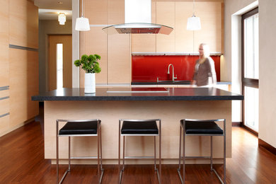 ミネアポリスにあるコンテンポラリースタイルのおしゃれなアイランドキッチン (フラットパネル扉のキャビネット、淡色木目調キャビネット、赤いキッチンパネル、ガラス板のキッチンパネル、パネルと同色の調理設備、濃色無垢フローリング) の写真