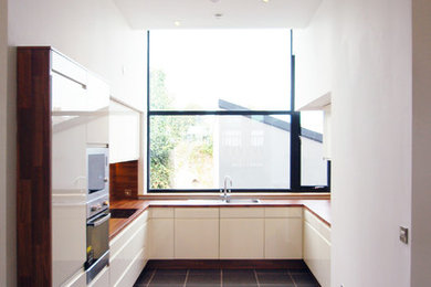 Mittelgroße Moderne Wohnküche ohne Insel in U-Form mit flächenbündigen Schrankfronten, beigen Schränken, Laminat-Arbeitsplatte und Küchengeräten aus Edelstahl in Cork