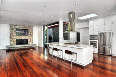 Example of a large minimalist l-shaped dark wood floor eat-in kitchen design in Orange County with flat-panel cabinets, white cabinets, marble countertops, white backsplash, stainless steel appliances, a peninsula and a double-bowl sink