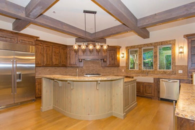 Example of a mid-sized classic l-shaped light wood floor and brown floor eat-in kitchen design in Portland with a farmhouse sink, raised-panel cabinets, medium tone wood cabinets, granite countertops, beige backsplash, stone tile backsplash, stainless steel appliances and an island